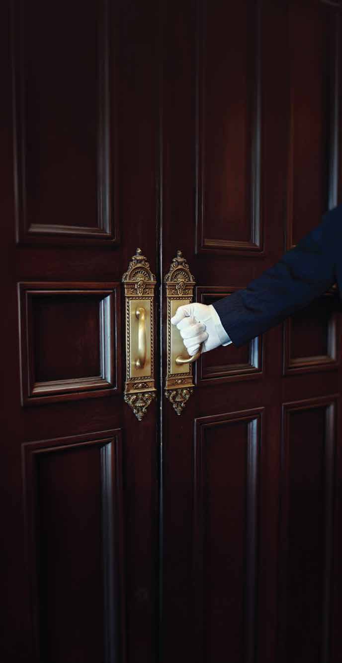 White-gloved concierge opening carved double doors